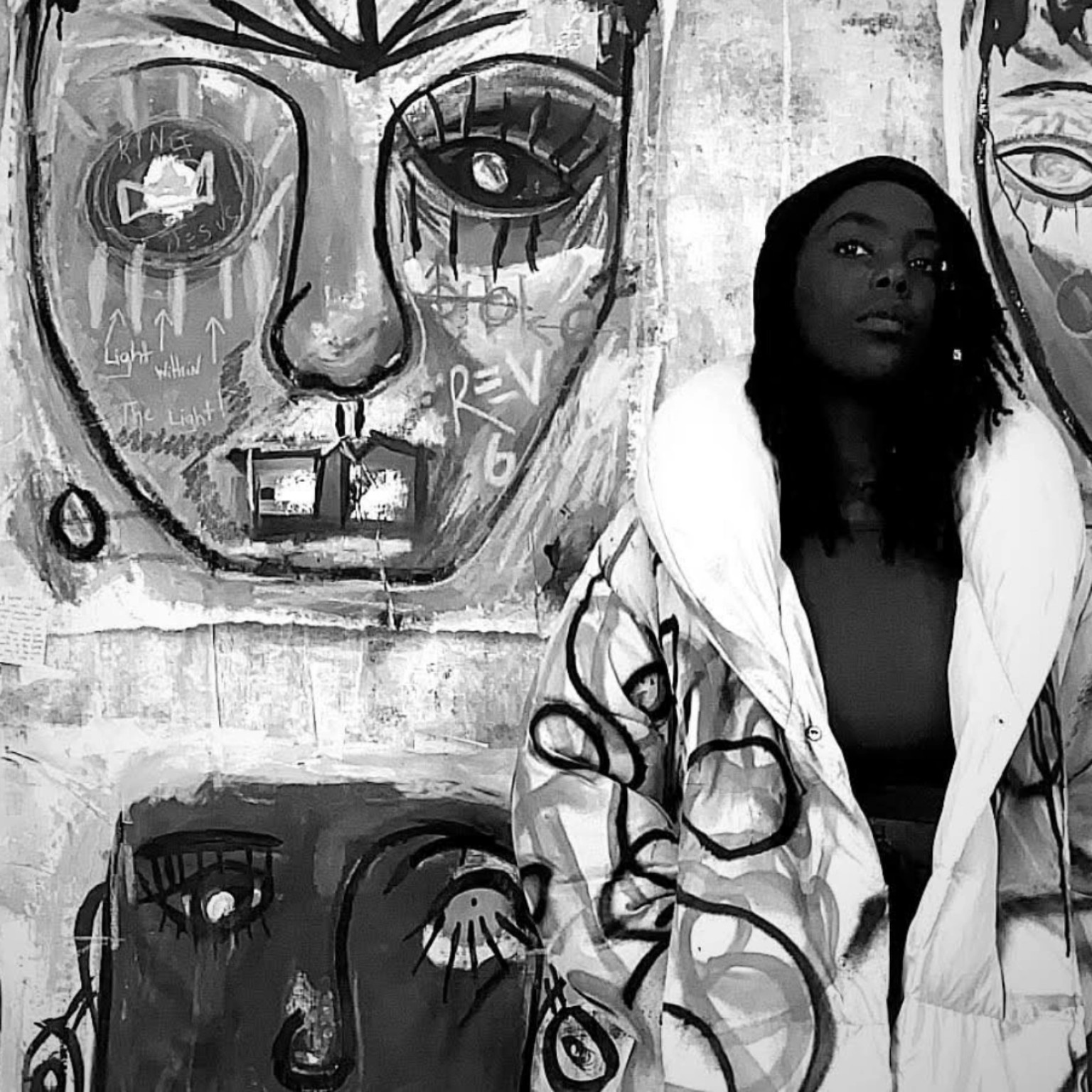 Black and white portrait of ENNÈ seated in front of her artwork